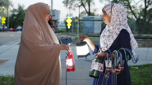 Two women in hijabs talking and holding camping lamps.