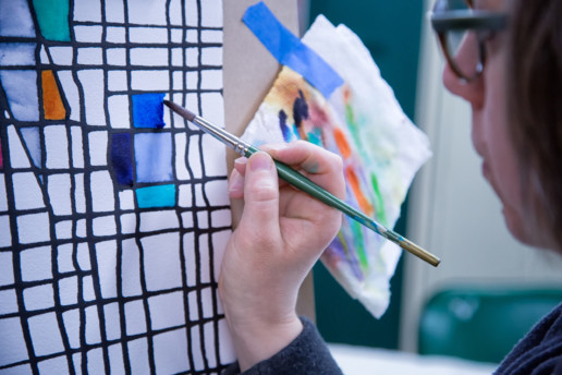 Jes Reyes, a woman with short brown hair, paints a colorful grid